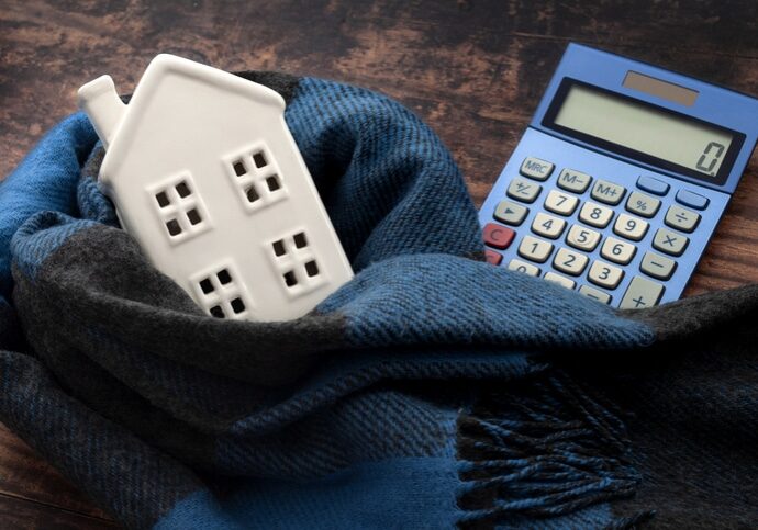 Warming efficiency of a residence and calculate heating costs concept with digital calculator, small house wrapped in warm wool neck scarf on wood background