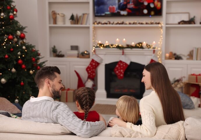 Happy family spending time on sofa near TV in cosy room, back view. Christmas atmosphere